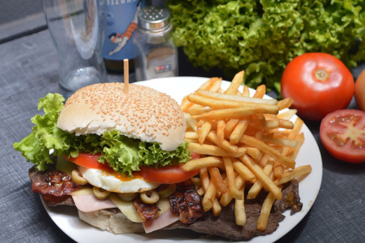 American Burger mit Pommes, Salat, Tomaten und Sesambrötchen auf einem Teller